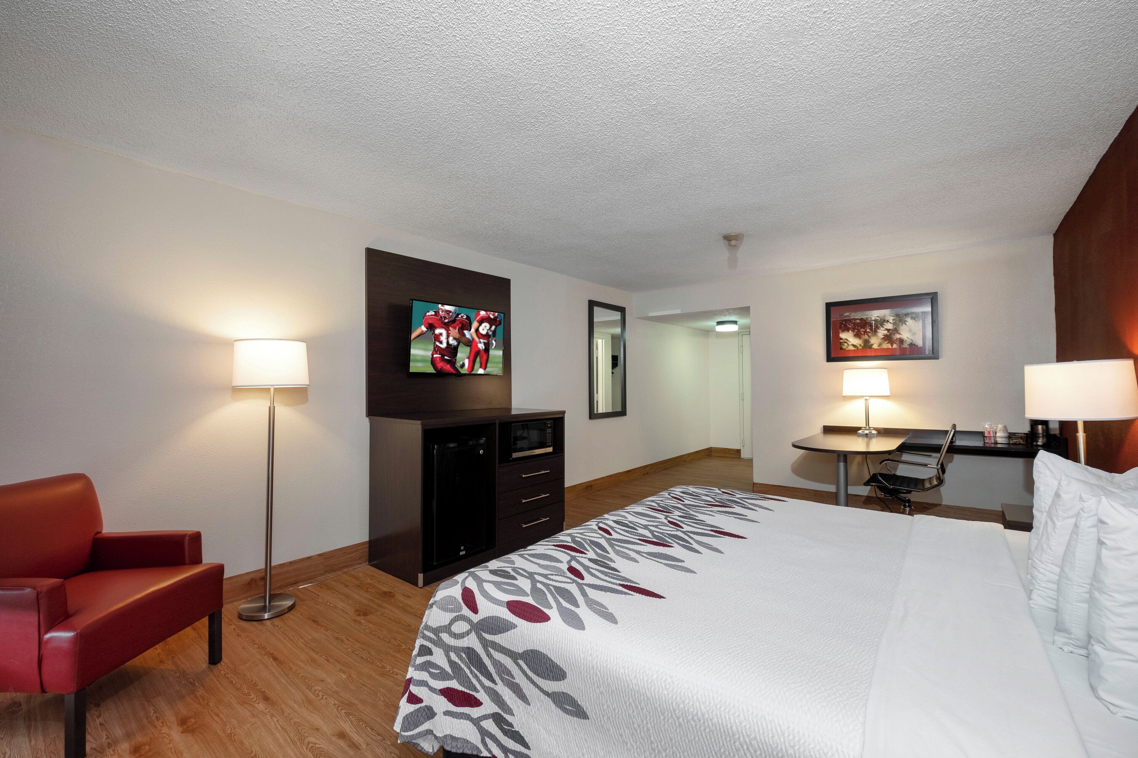 A hotel room with a bed, a desk, a chair, a TV, and a lamp.