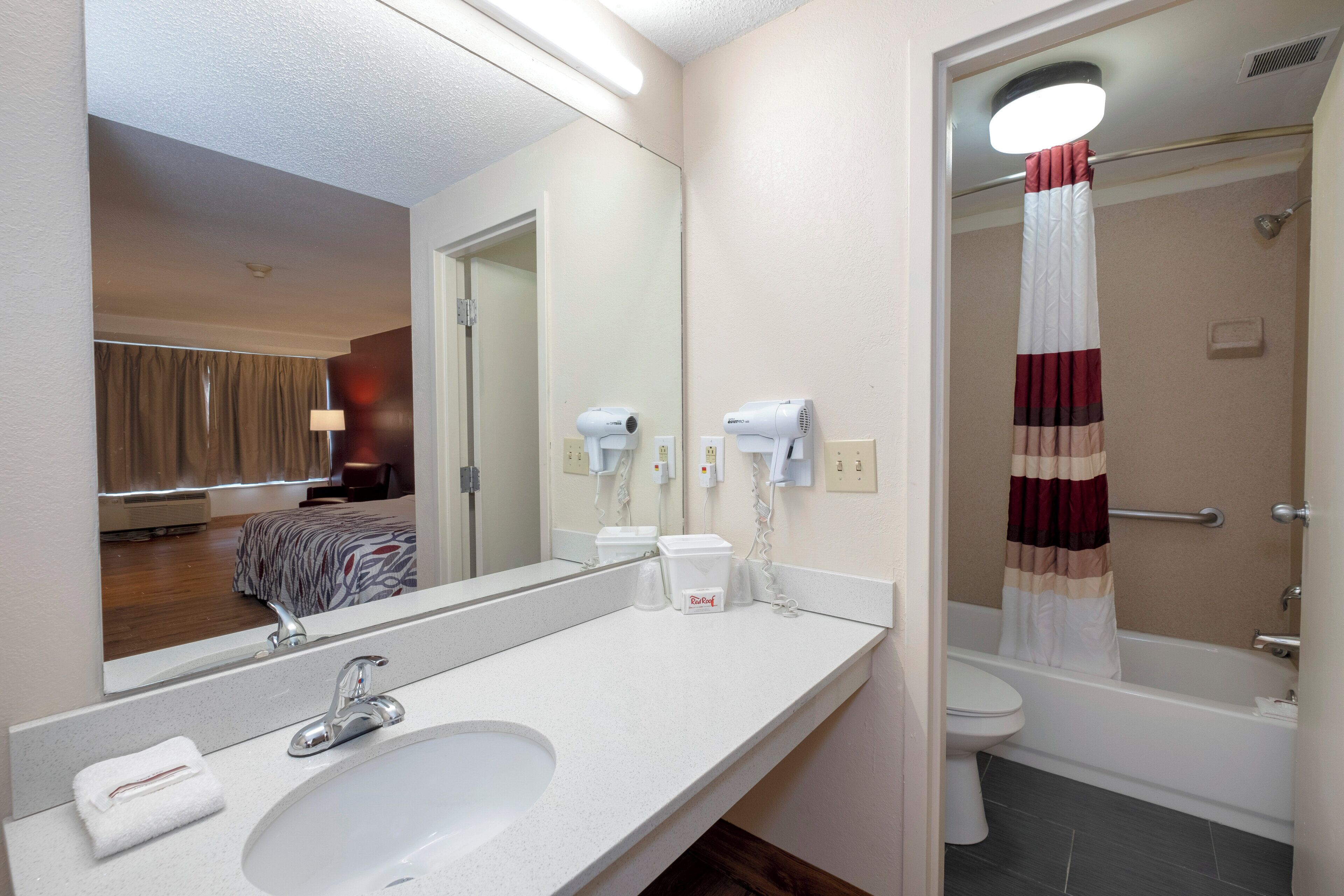 Een hotelbadkamer met een wastafel, spiegel, handdoek en een douche met gordijn.