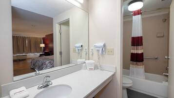 Een hotelbadkamer met een wastafel, spiegel, handdoek en een douche met gordijn.