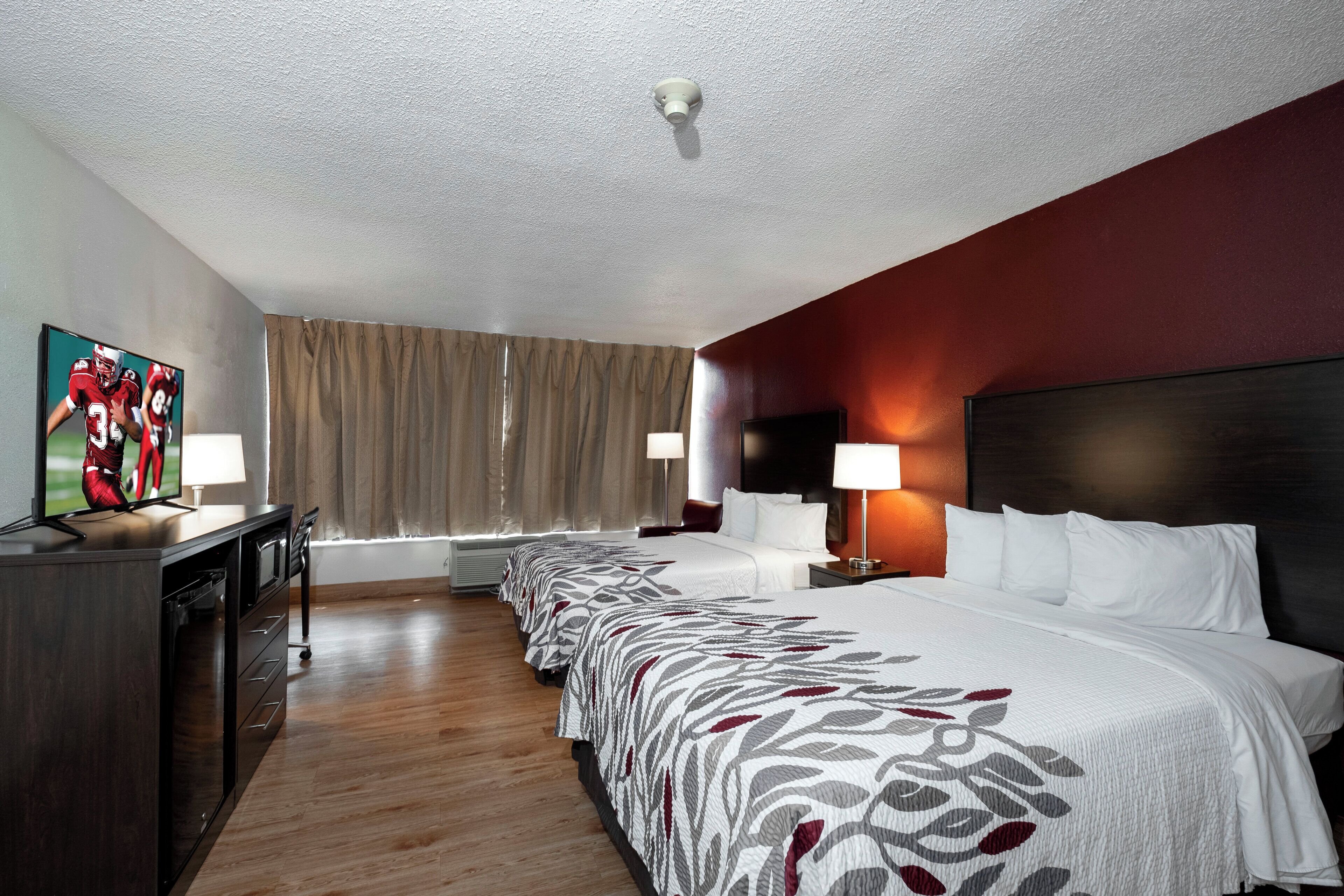 A hotel room with a bed, a desk, a TV, and a window with curtains.