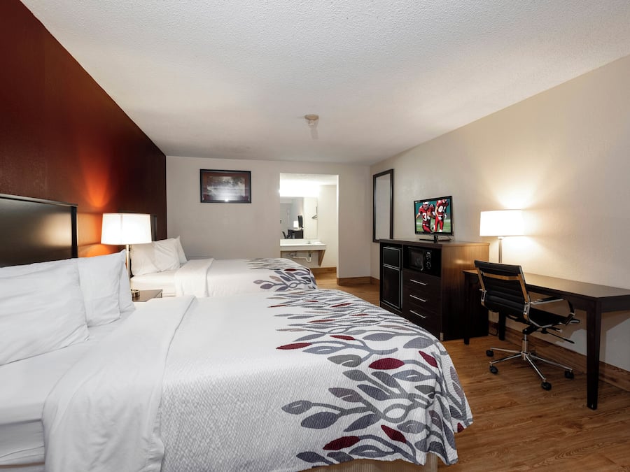 Ein Hotelzimmer mit einem großen Bett, einem Schreibtisch, einem Sessel, einem Fernseher und einem im Hintergrund sichtbaren Badezimmer.