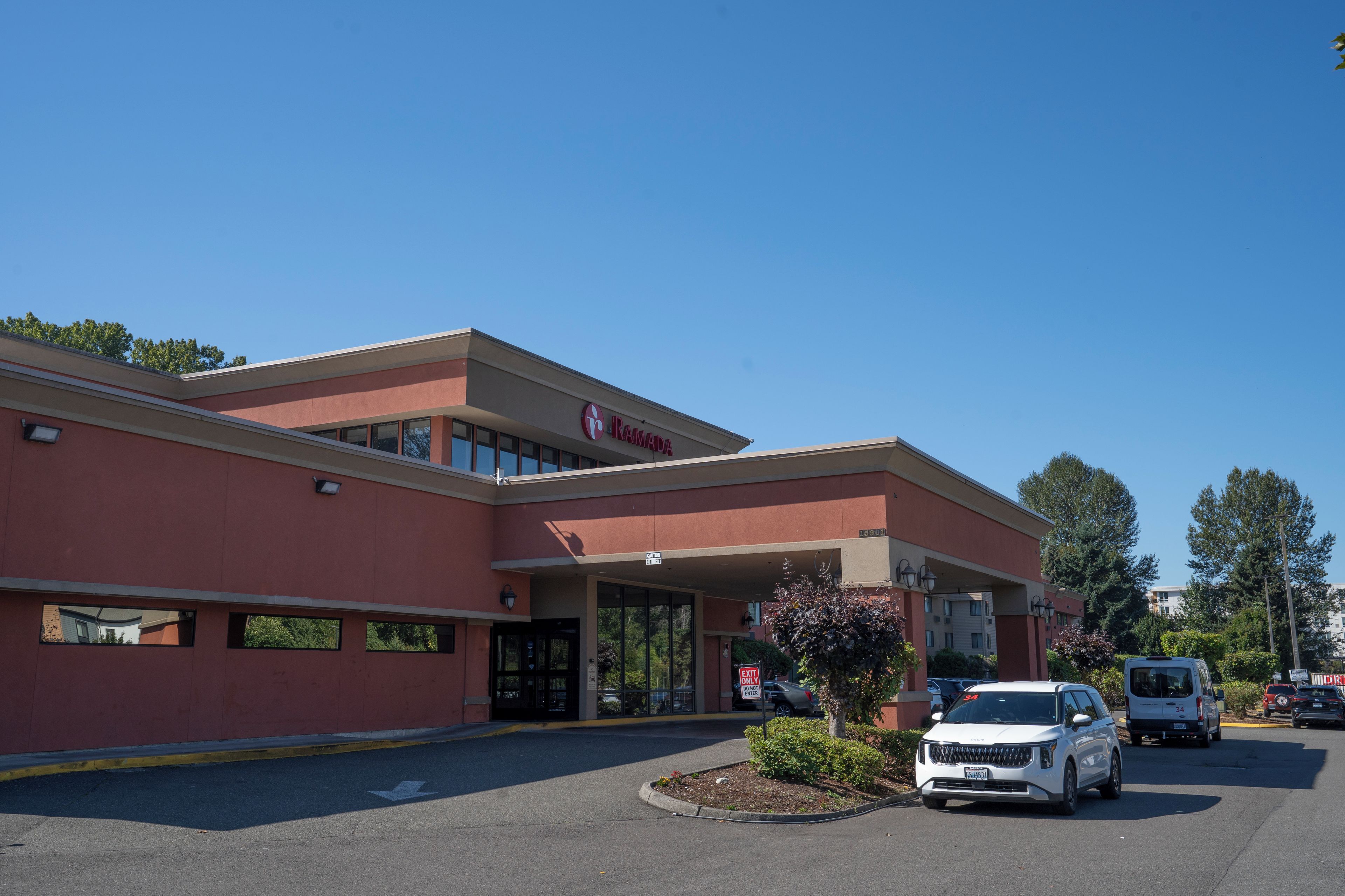 A commercial building with a sign reading 'RAMADA' and a parking lot with several vehicles.
