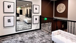 Un vestíbulo de hotel con un espejo grande, obras de arte enmarcadas, un sofá blanco y una escalera con barandilla.