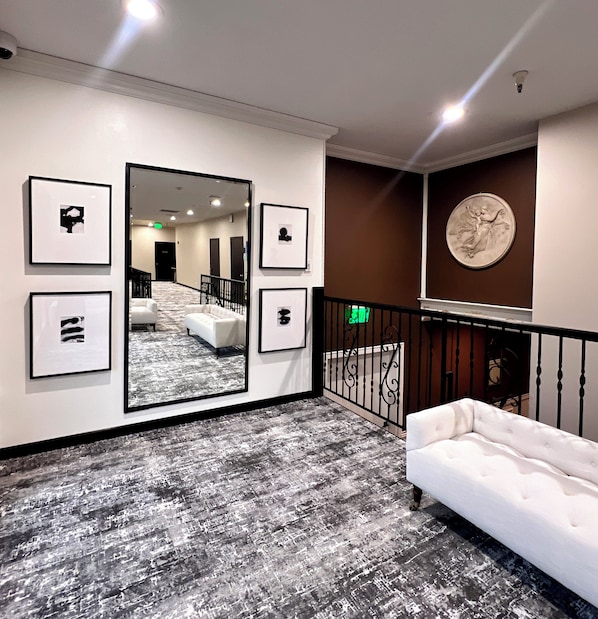 Un vestíbulo de hotel con un espejo grande, obras de arte enmarcadas, un sofá blanco y una escalera con barandilla.