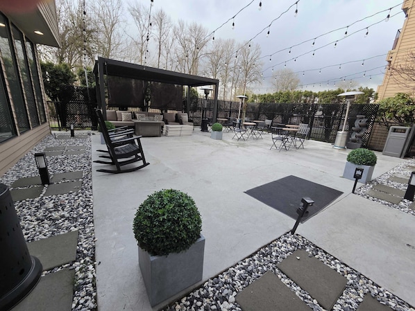 Un patio al aire libre con mobiliario, una pérgola y luces colgantes.