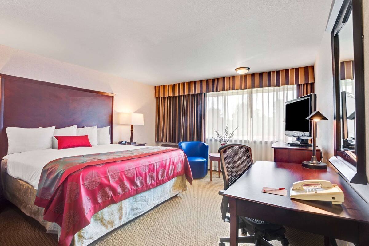 Een hotelkamer met een bed, bureau, stoel, televisie en een raam met gordijnen.