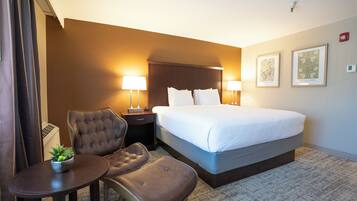 A hotel room with a large bed, two bedside lamps, a chair, a small table with a plant, and two framed artworks on the wall.