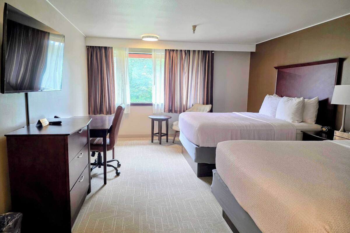 Een hotelkamer met twee bedden, een bureau, een stoel, een televisie en een raam met gordijnen.
