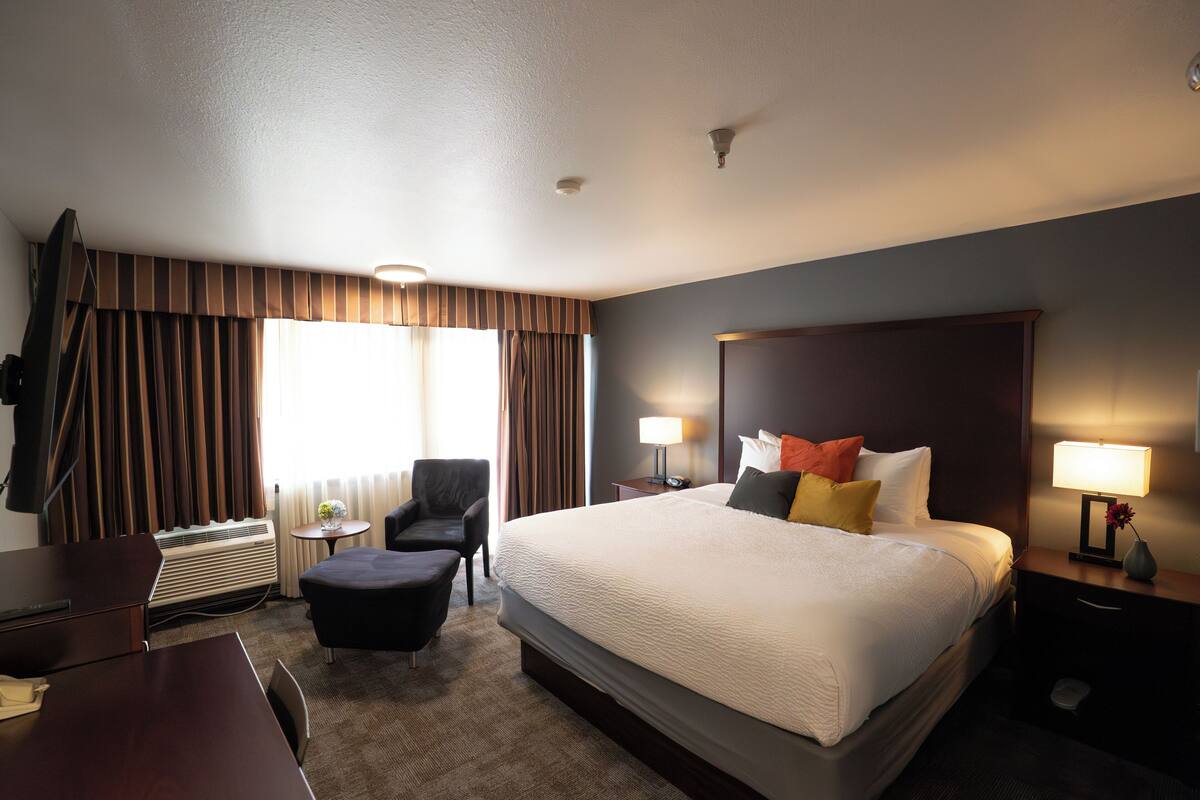 Een hotelkamer met een groot bed, een bureau, een stoel en een klein tafeltje met een lamp.