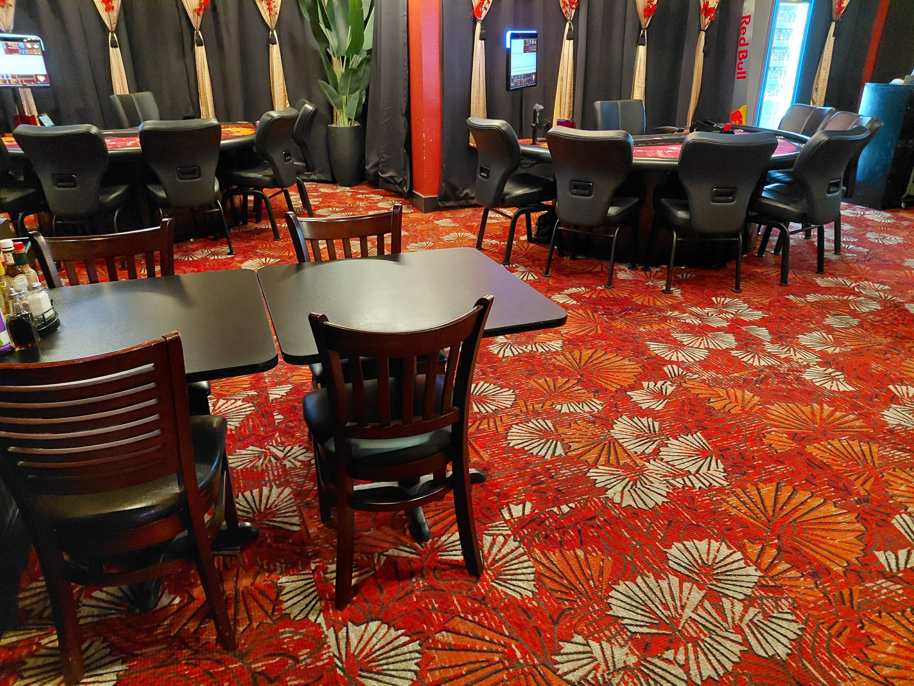 A hotel room with a red patterned carpet, wooden chairs, and tables.
