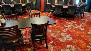 A hotel room with a red patterned carpet, wooden chairs, and tables.