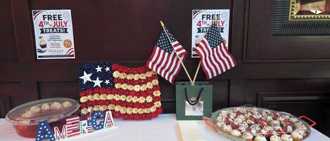 A table with American flags, a sign offering free treats, and a display of cupcakes.