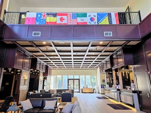 A hotel lobby with a reception desk, seating area, and a ceiling with a grid pattern. Flags are displayed above the reception. - Ramada by Wyndham Tukwila Southcenter (Tukwila)