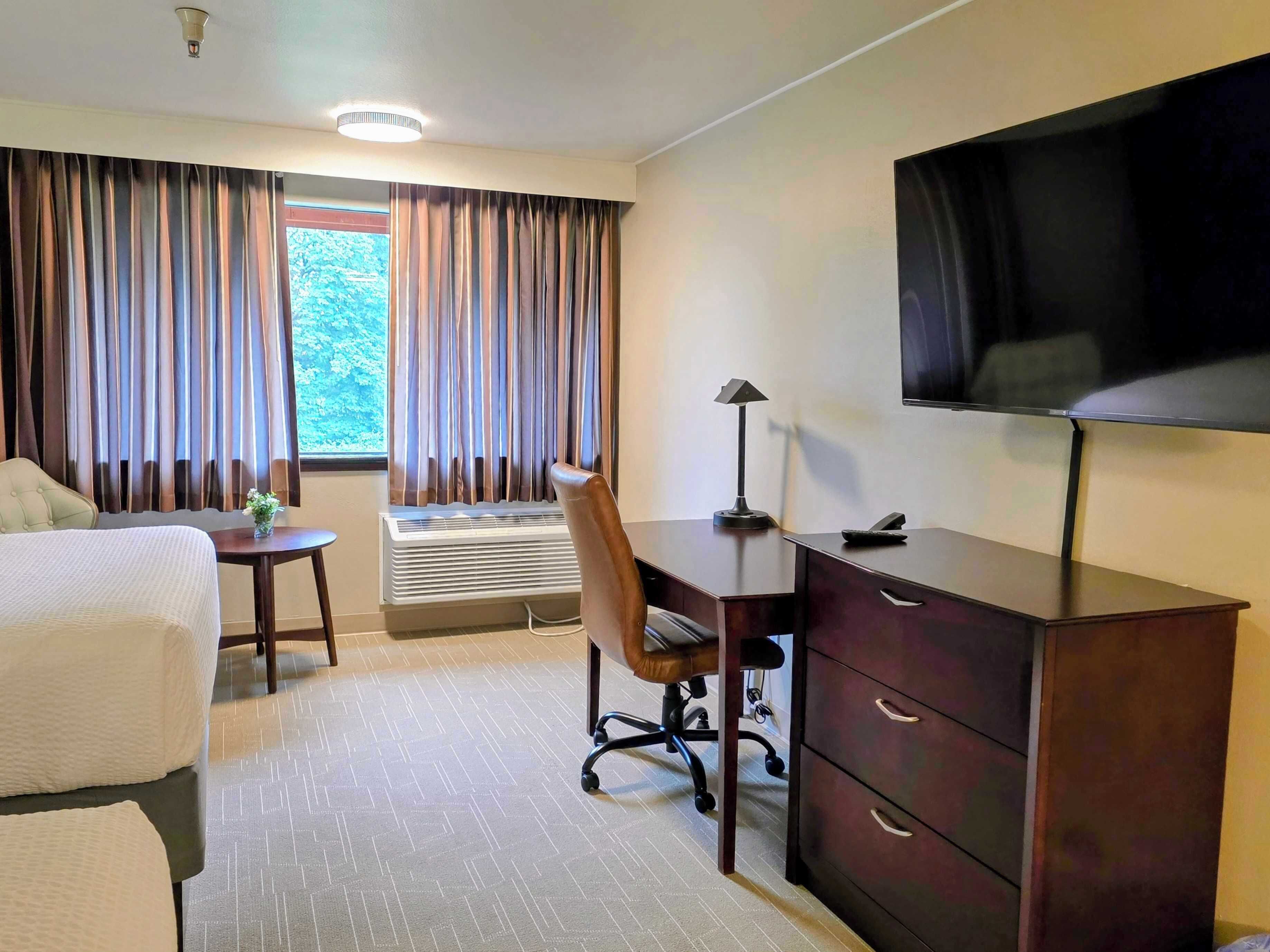 Une chambre d’hôtel équipée d’un lit, d’un bureau, d’une chaise, d’une télévision et d’une fenêtre avec des rideaux.