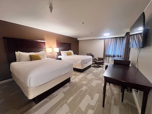 Habitación de hotel con dos camas, un escritorio, una silla, una lámpara, un televisor y una ventana con cortinas.