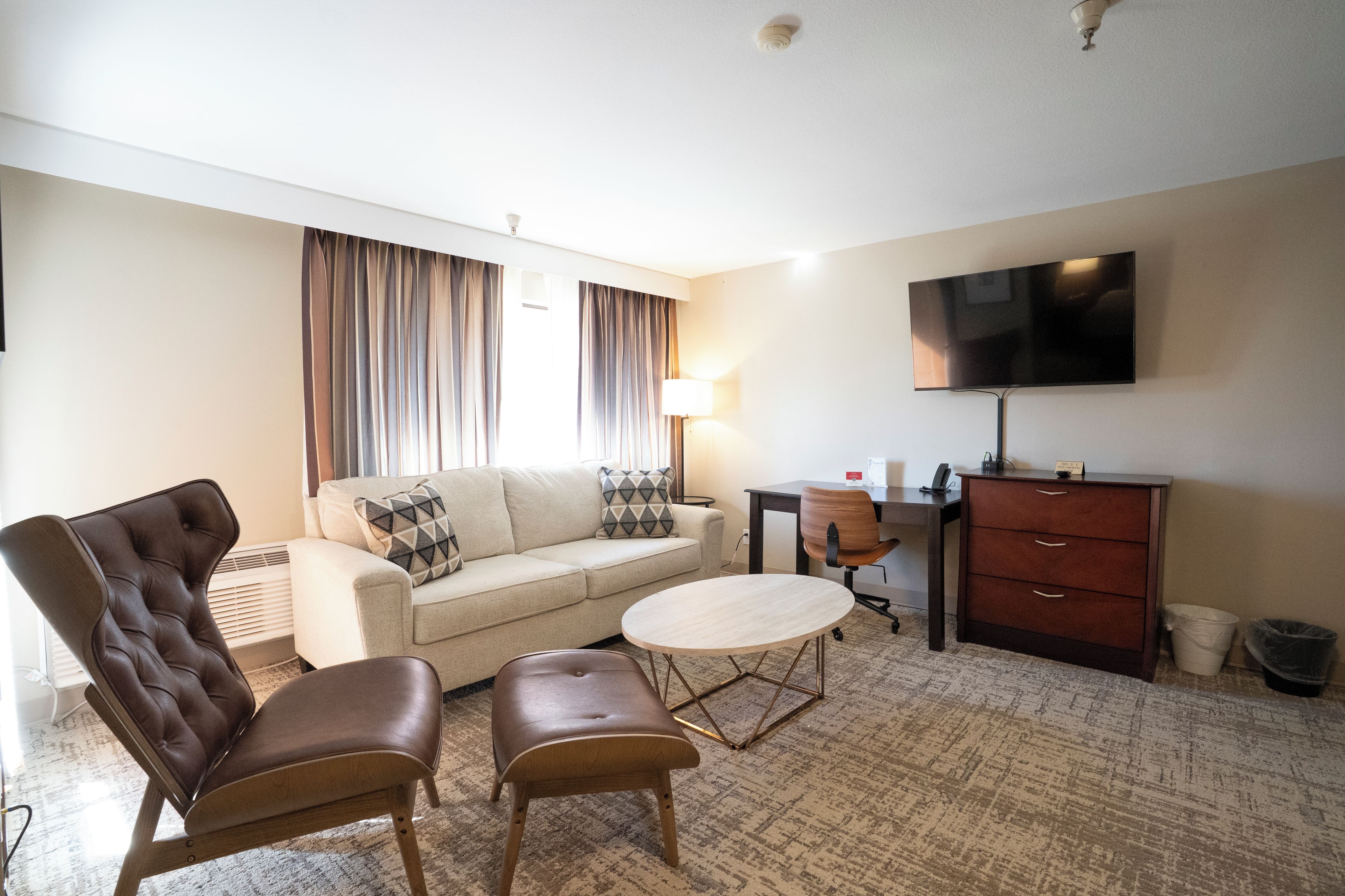 Een hotelkamer met een bank, twee fauteuils, een salontafel, een bureau, een televisie en een prullenbak.