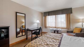 Una habitación de hotel con cama, escritorio, silla y un espejo grande.