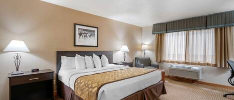 A hotel room with a large bed, two bedside tables, a chair, a desk, a framed picture on the wall, and a window with curtains.