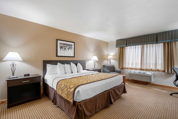 Ein Hotelzimmer mit einem großen Bett, zwei Nachttischen, einem Sessel, einem Schreibtisch, einem gerahmten Bild an der Wand und einem Fenster mit Vorhängen.