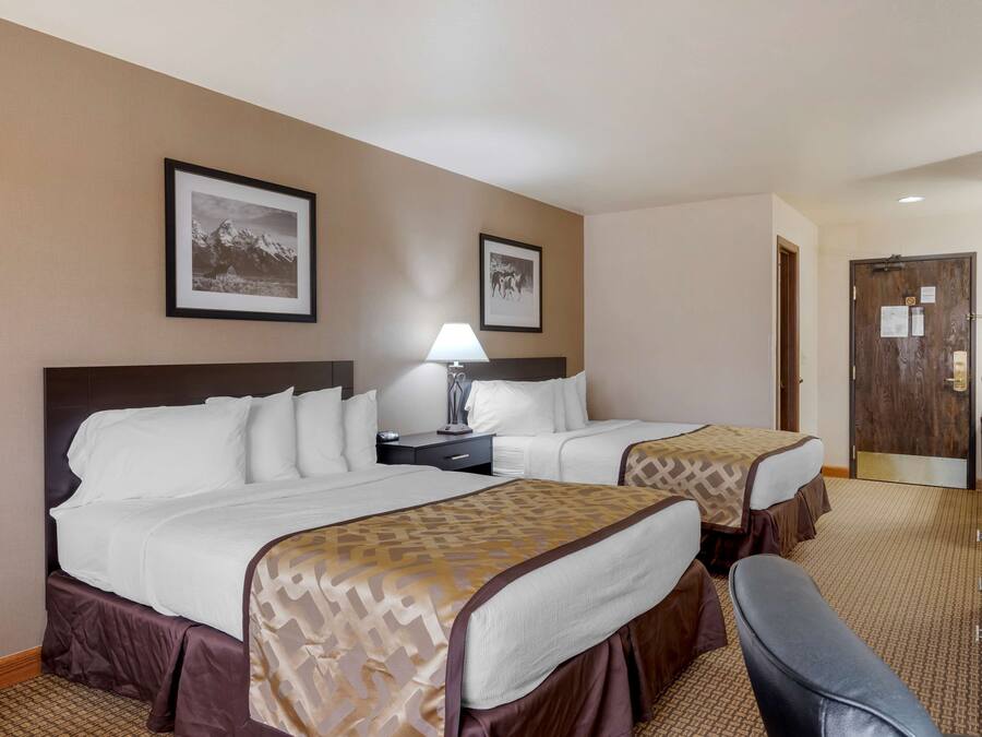 A hotel room with two beds, a desk, a chair, and a door.