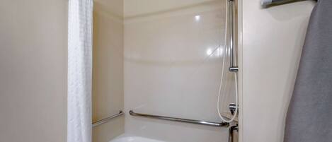 A shower area with a grab bar, a white bathtub, and a towel rack.