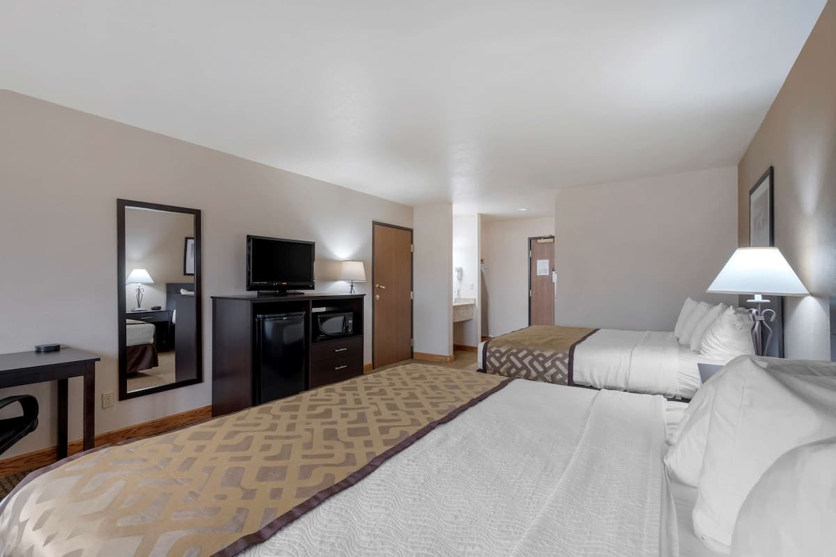 A hotel room with two beds, a desk, a television, and a mirror.