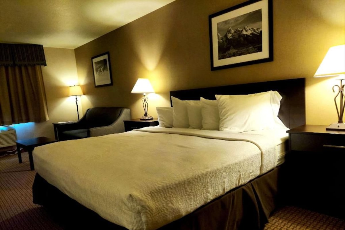 A hotel room with a large bed, two bedside tables, a chair, and a framed picture on the wall.