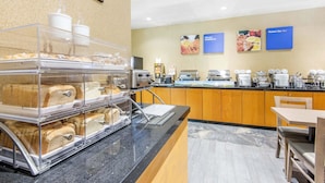 Un bufé de desayuno con panadería, una estación de café y un área de estar con mesas y sillas de madera.