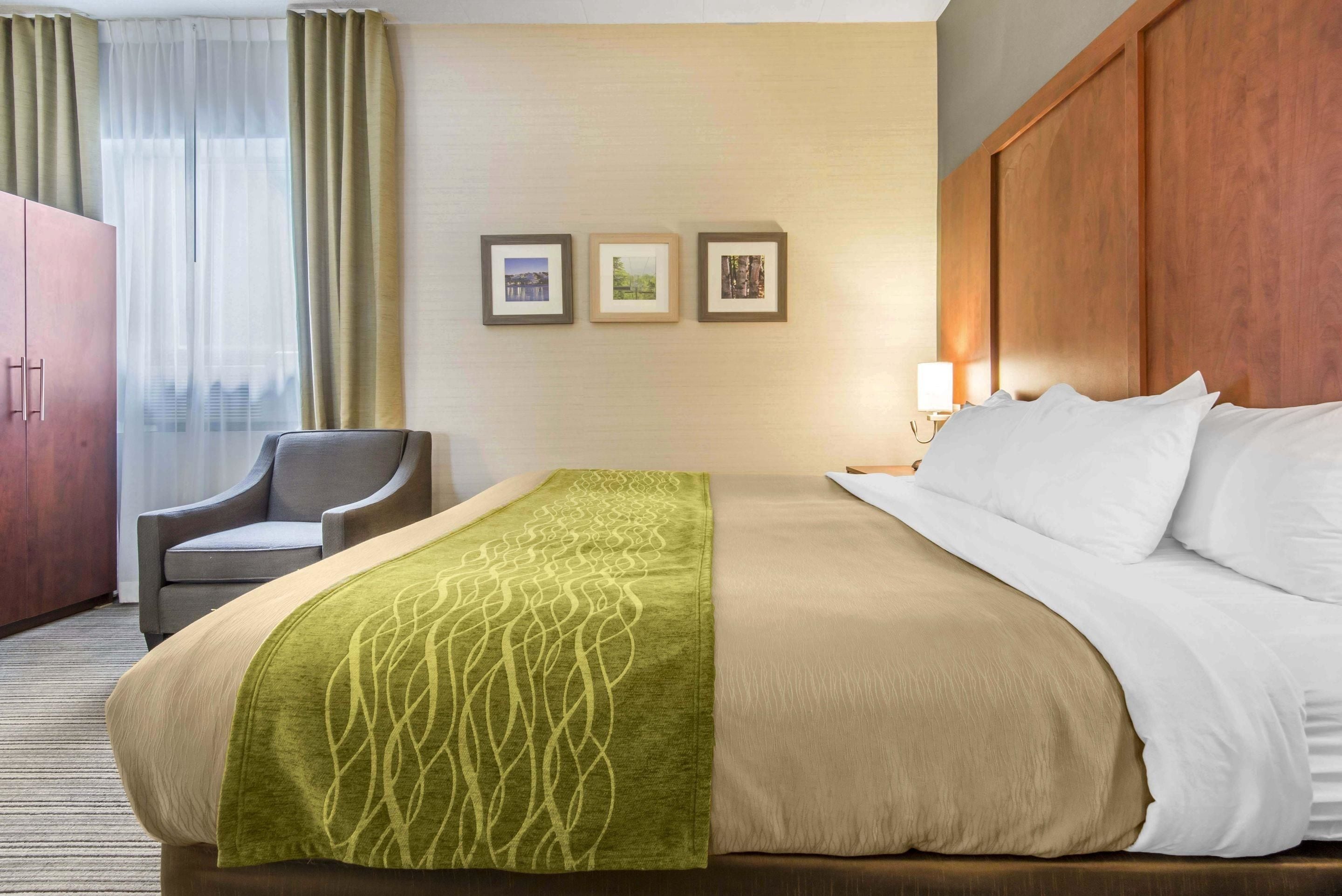 A hotel room with a bed, a chair, a wardrobe, and three framed pictures on the wall.