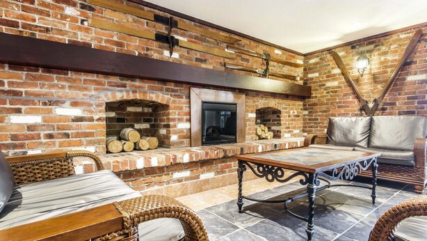 Una chimenea de ladrillo con leña, suelo de baldosas de piedra, muebles de mimbre y una mesa de madera oscura.
