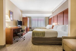Quarto de hotel com cama, escrivaninha com computador, cadeira e televisão.