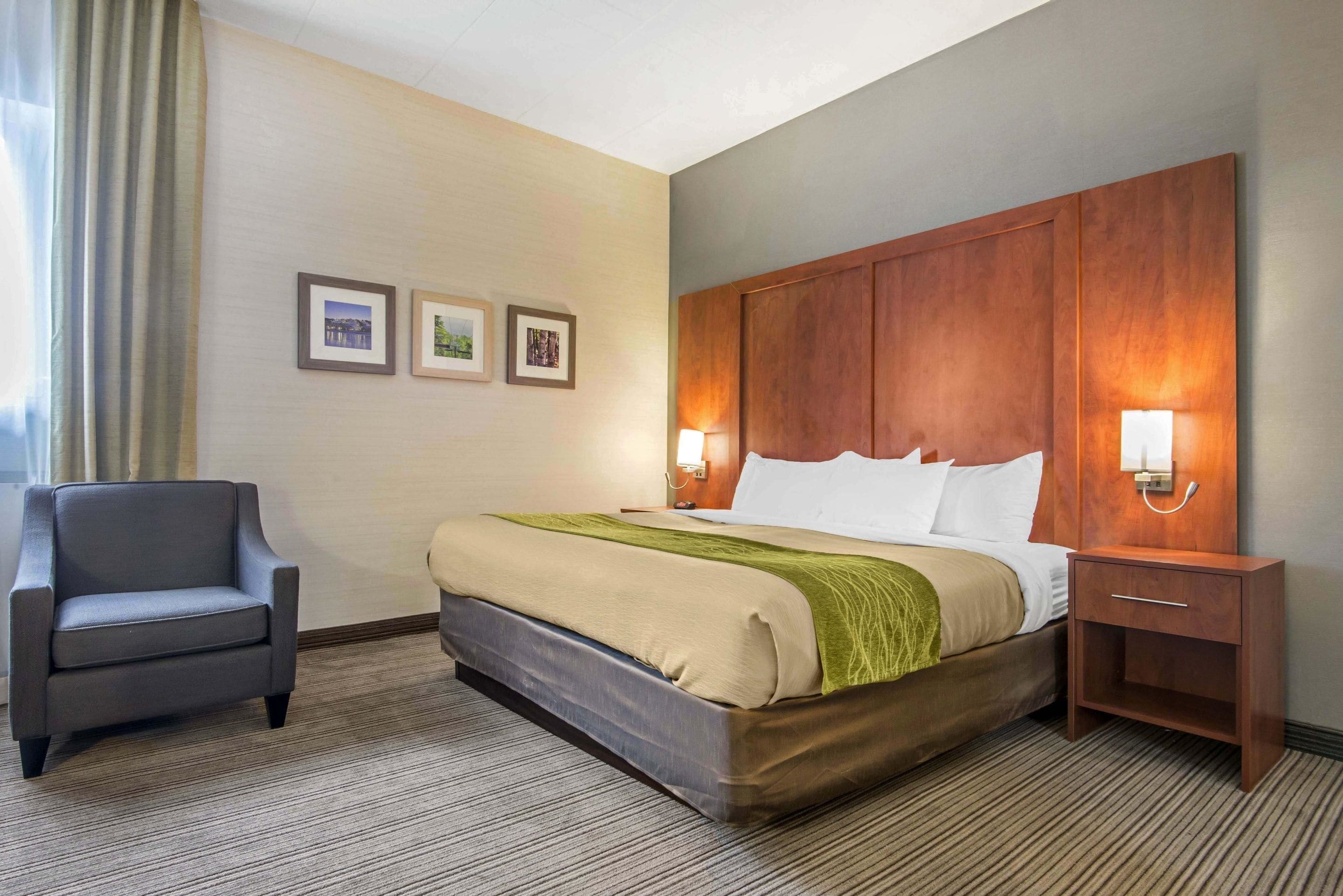 A hotel room with a bed, a chair, a nightstand, and three framed pictures on the wall.