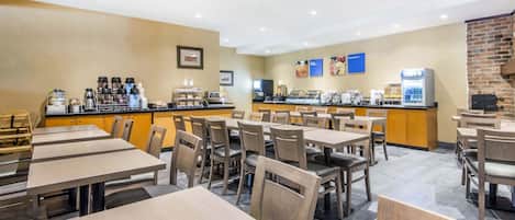A hotel dining area with multiple tables and chairs, a coffee station, and a counter with food and beverage options.