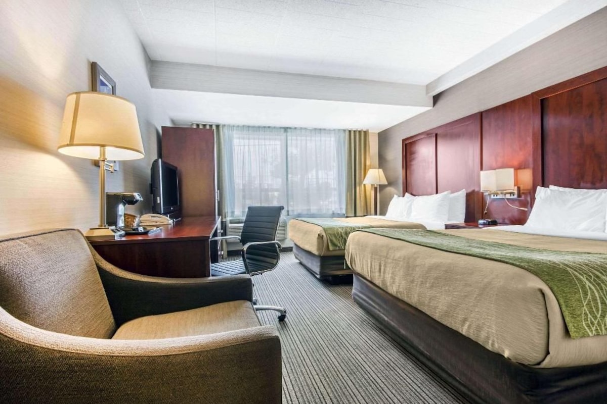 A hotel room with a bed, two bedside tables, a desk with a lamp, a chair, and a television.