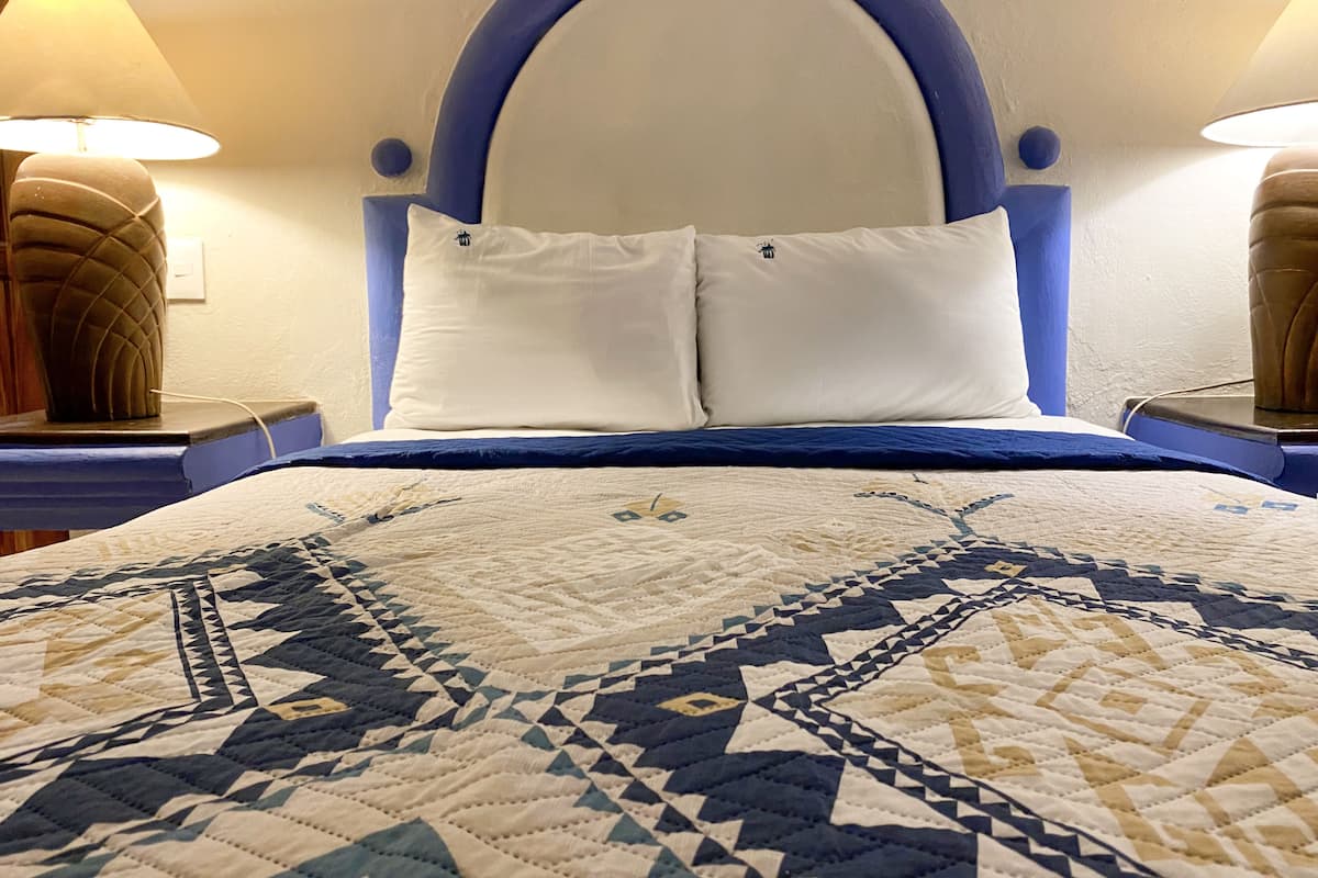 Ein ordentlich bezogenes Bett mit einer gemusterten Decke, einem blauen Kopfteil und zwei Nachttischlampen auf Holznächtigungstischen.