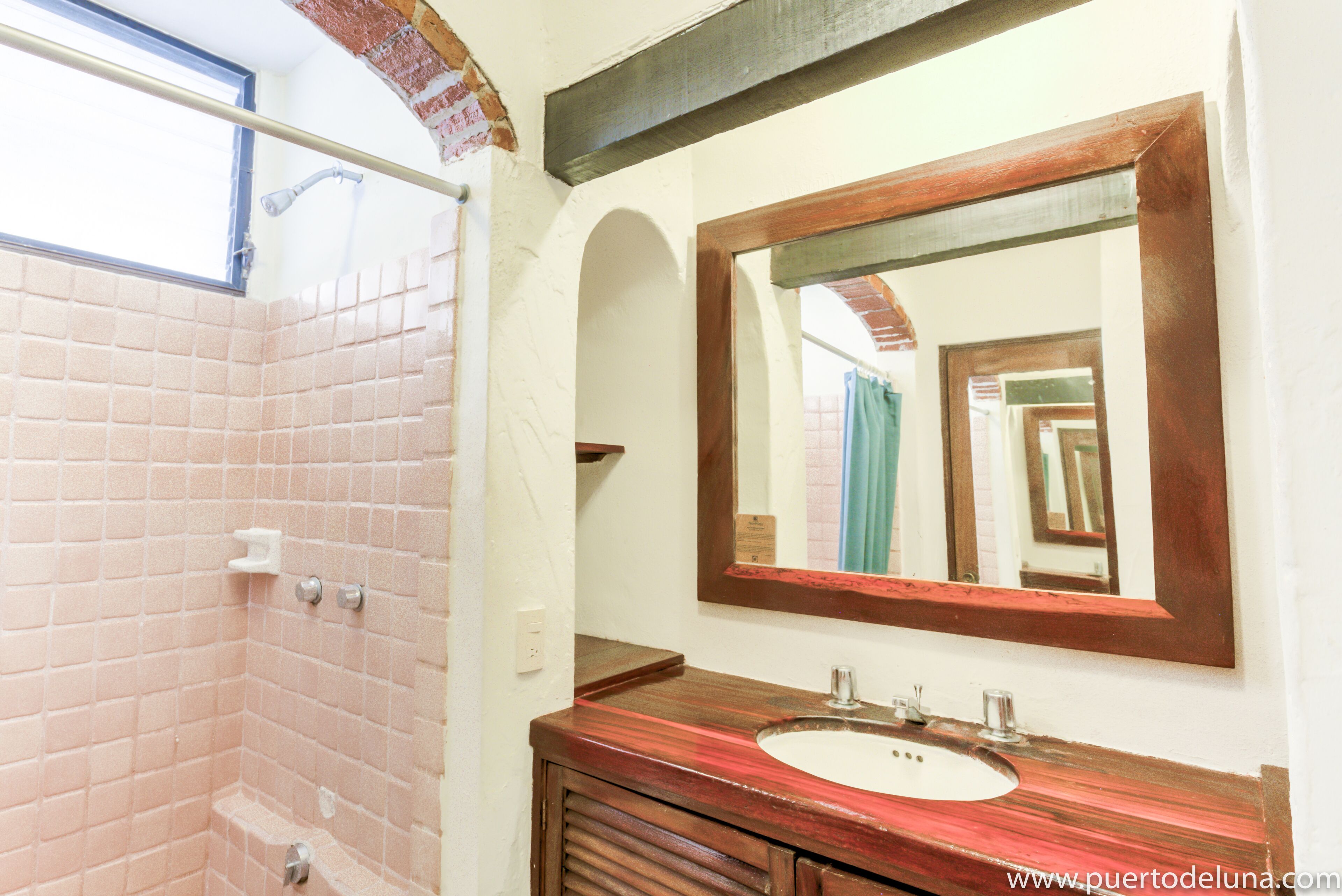 Une salle de bain avec une douche carrelée, un meuble-lavabo en bois et un grand miroir.