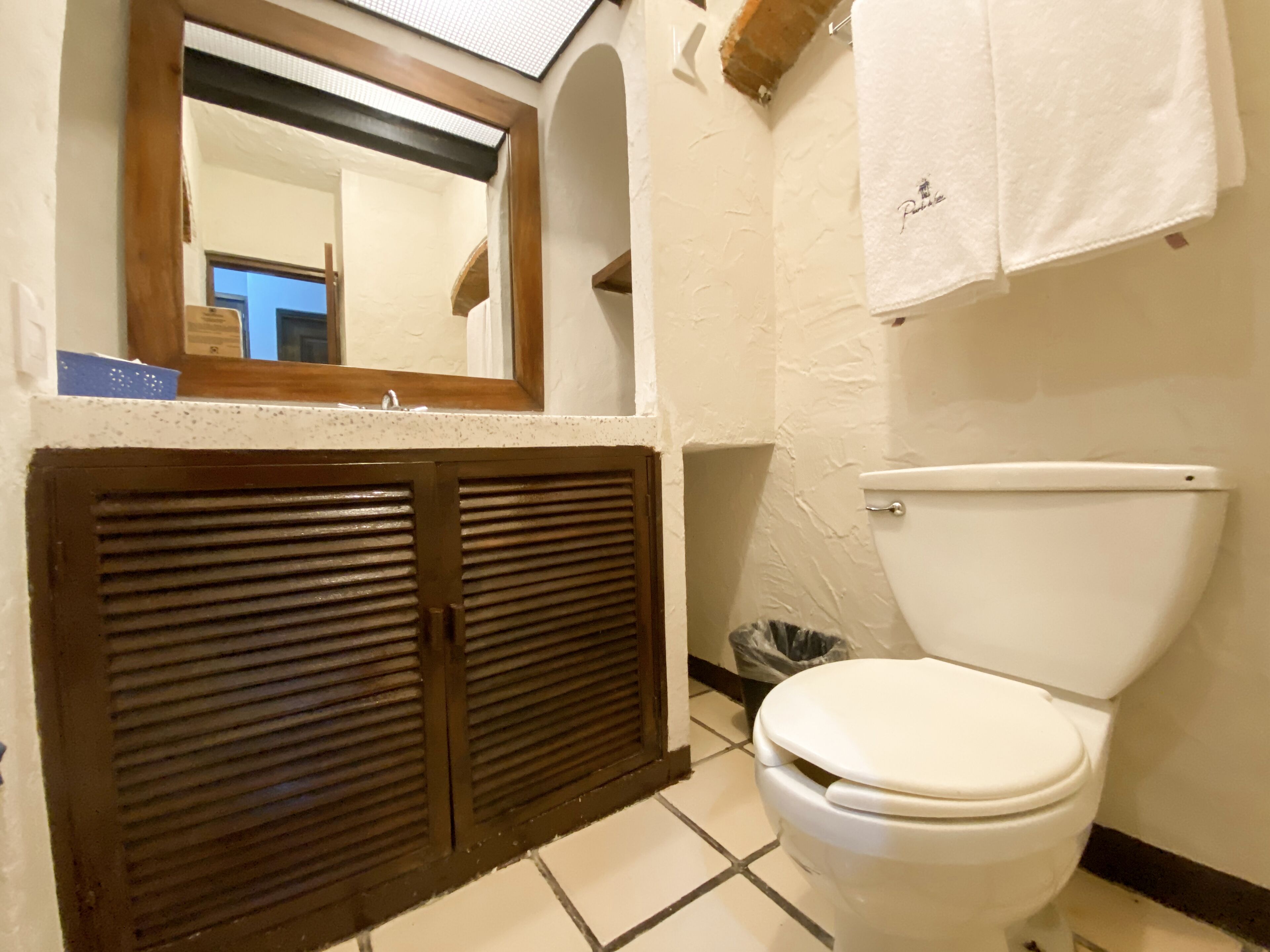 Un baño con inodoro, una ventana con marco de madera y una toalla colgada en la pared.