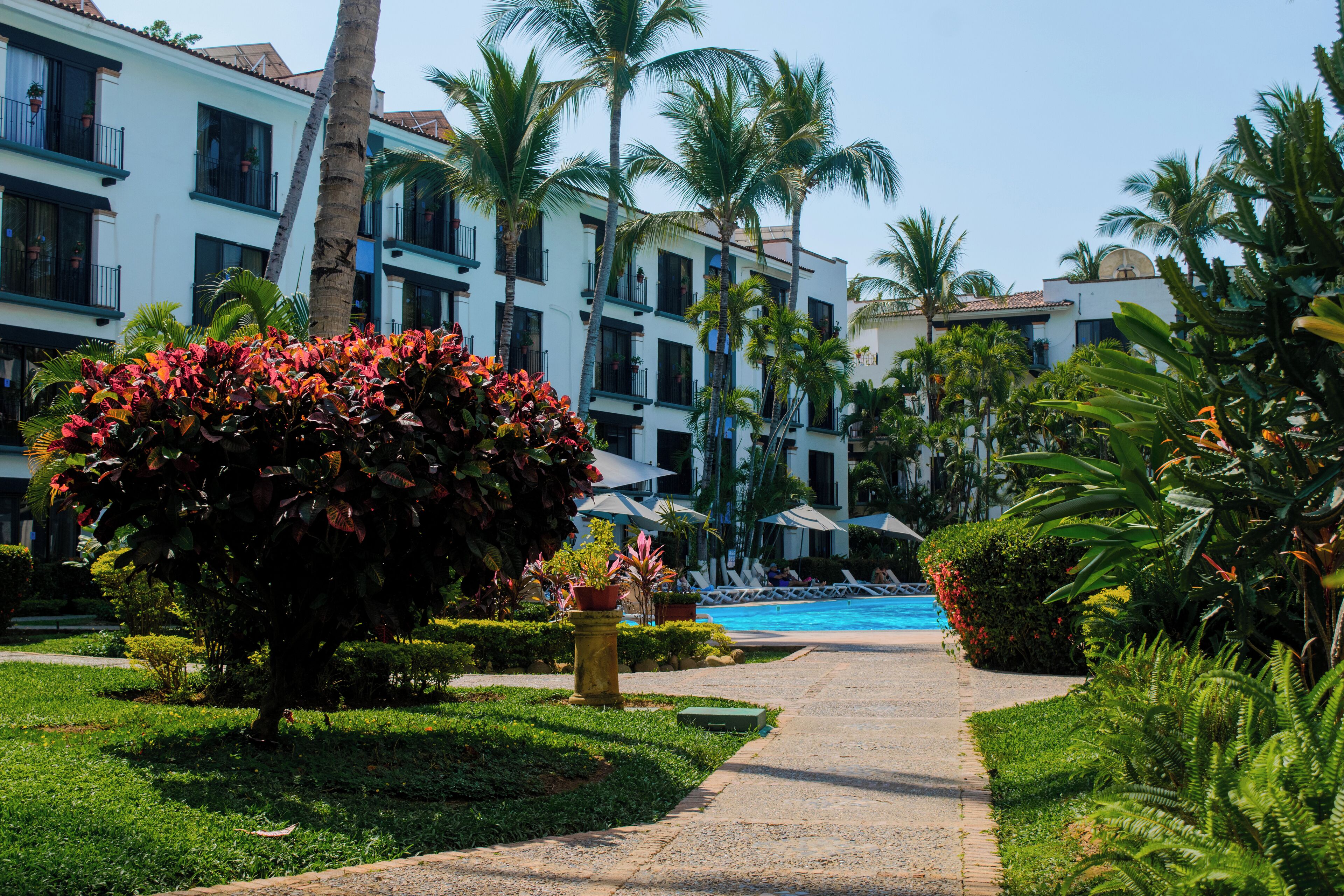 Un hôtel à étages, doté d’une piscine et entouré d’une végétation luxuriante, notamment de palmiers et de plantes à fleurs.