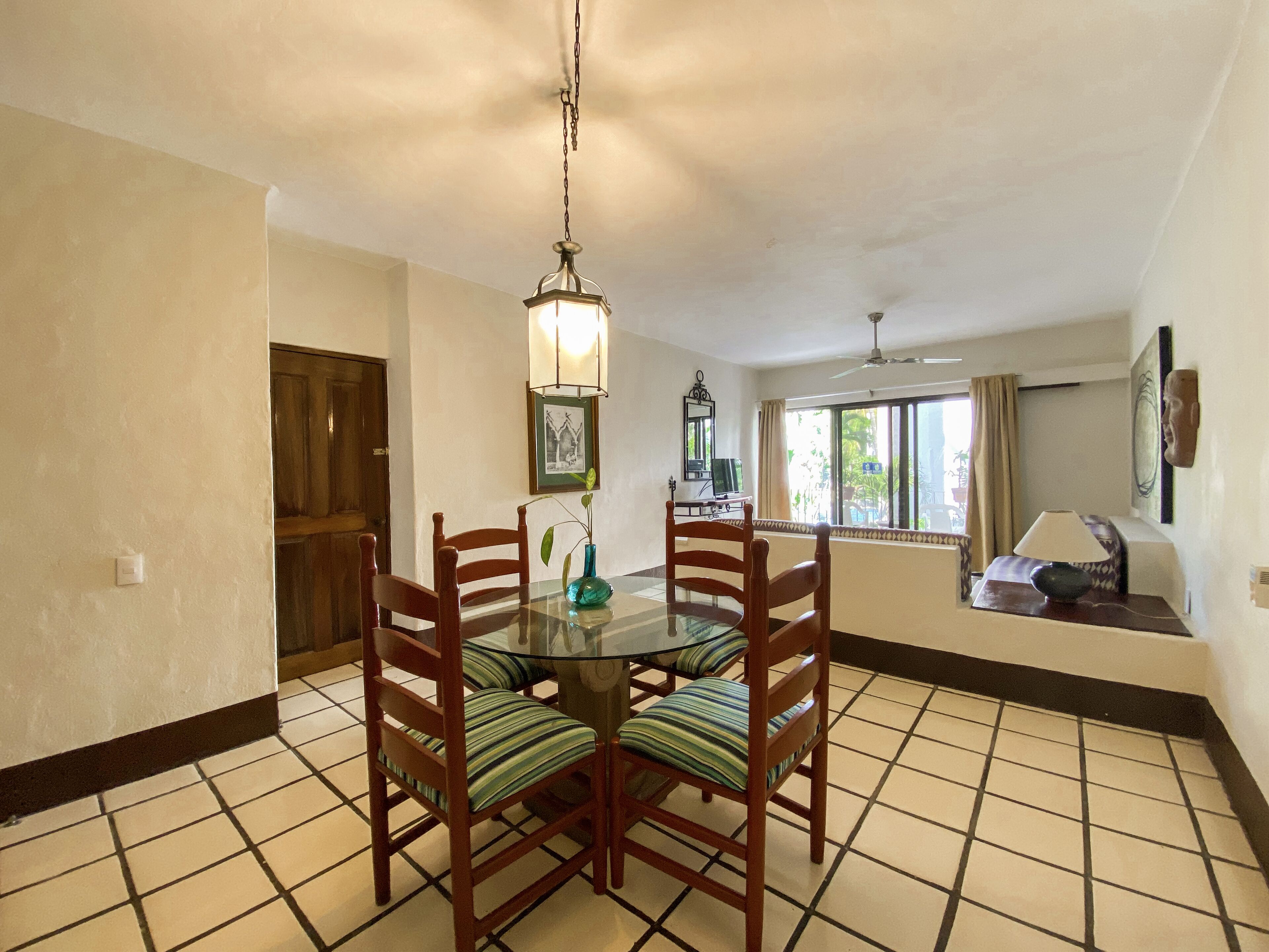A dining area with a round table, four chairs, a hanging light fixture, and a window with curtains.