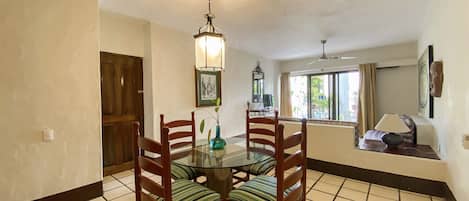 A dining area with a round table, four chairs, a hanging light fixture, and a window with curtains.