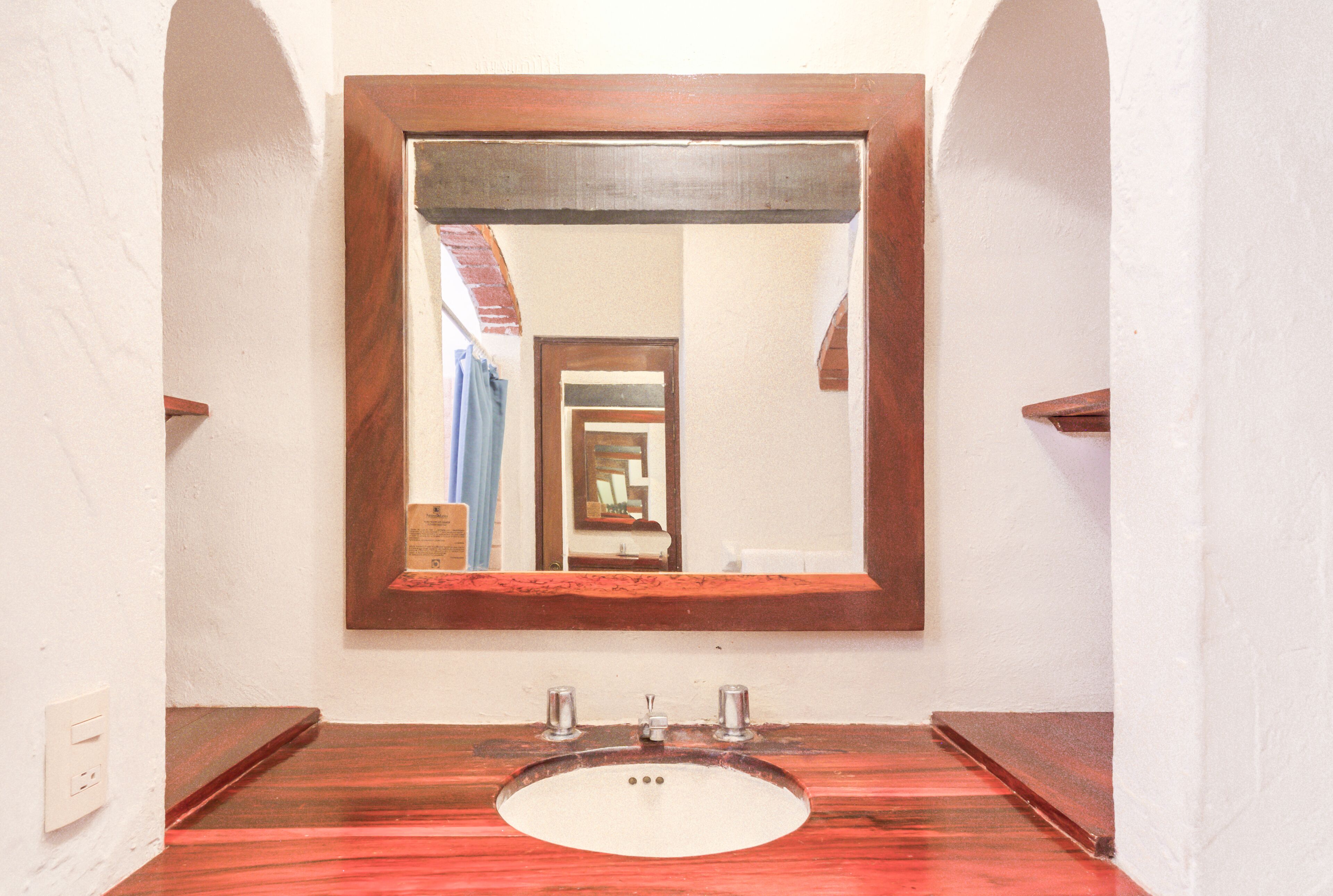 Ein Badezimmer mit einem spiegelnden Holzelement, einem weißen Waschbecken und einer roten Arbeitsfläche.