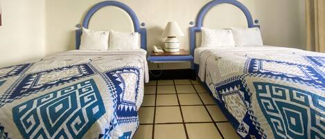 Een kamer met twee bedden, elk voorzien van een blauw hoofdeinde en witte beddengoed. Er is een wanddecoratie van een halve maan en een tekst die luidt: "La Luna te mueve la emoción".