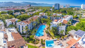 A resort with a central swimming pool, multiple buildings, and a view of the ocean and mountains in the background. - Puerto de Luna Pet Friendly & Family Suites Hotel (Puerto Vallarta)