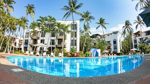 A hotel with a swimming pool surrounded by palm trees and a clear blue sky. - Puerto de Luna Pet Friendly & Family Suites Hotel (Puerto Vallarta)
