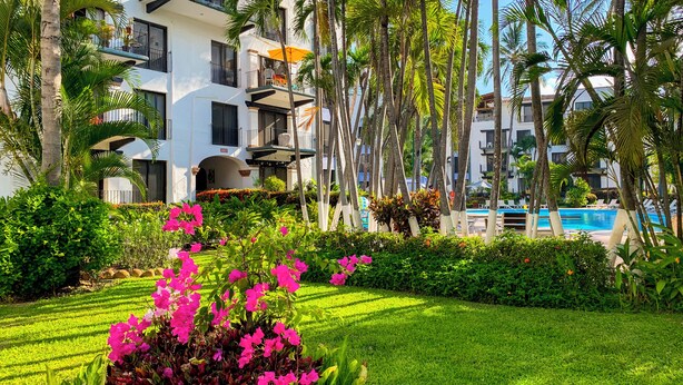 A hotel with multiple balconies, a swimming pool, and lush greenery. - Puerto de Luna Pet Friendly & Family Suites Hotel (Puerto Vallarta)
