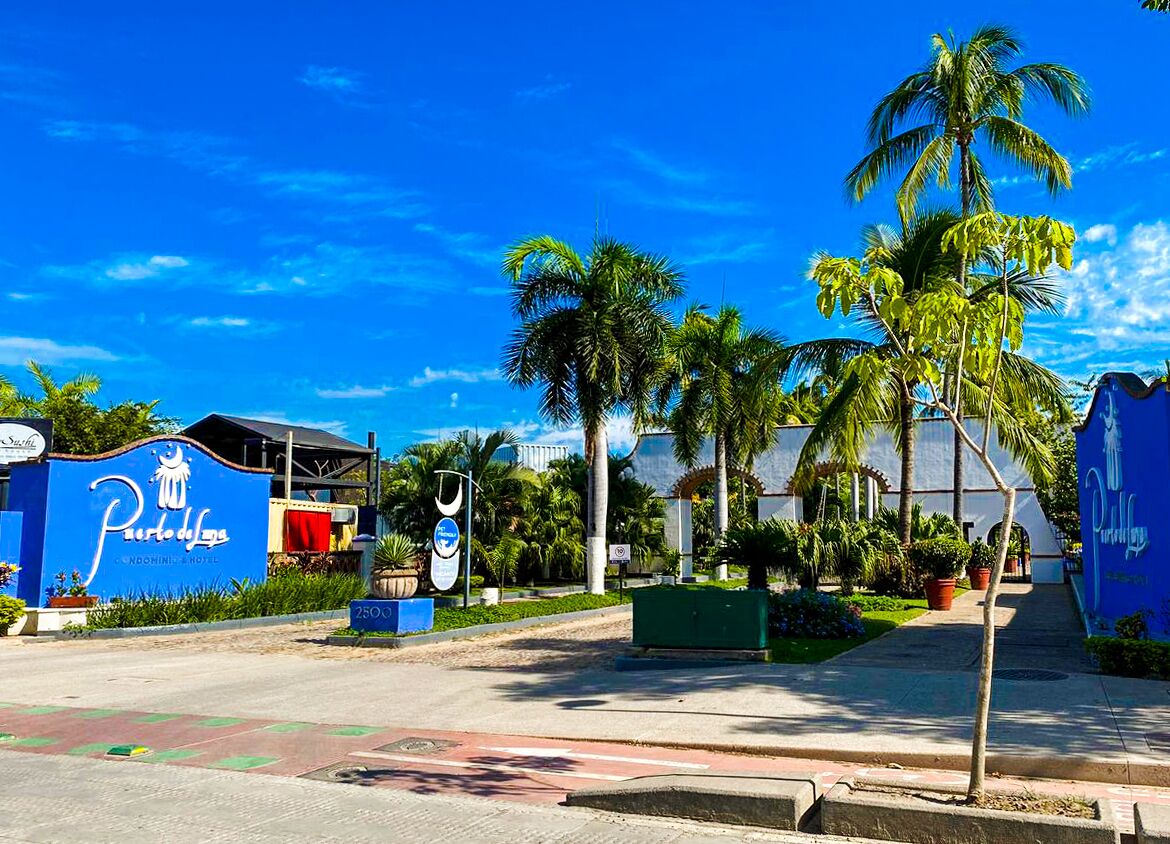A hotel entrance with a blue sign, palm trees, and a clear blue sky.