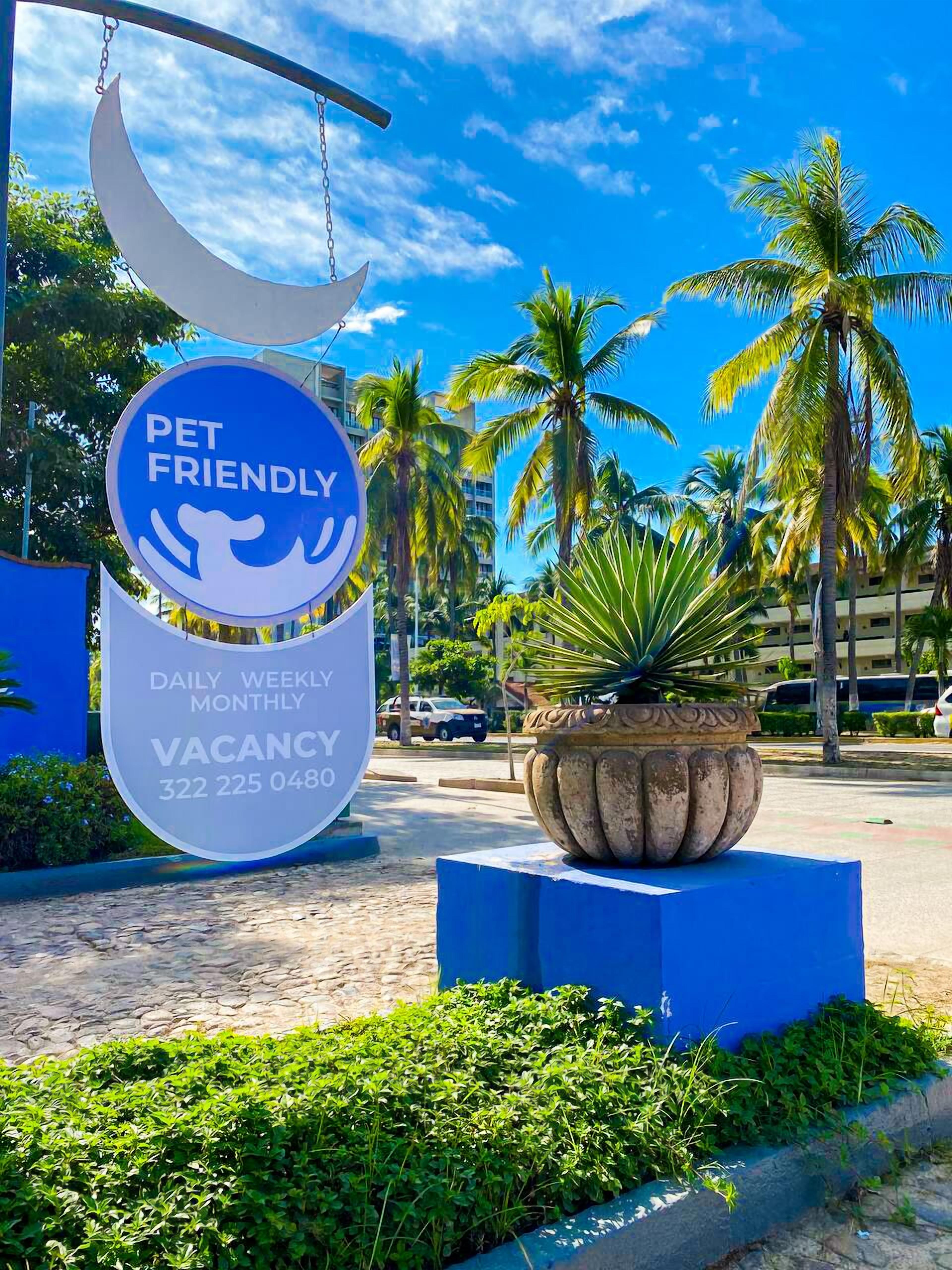 A pet-friendly vacation rental sign with a crescent moon, palm trees, and a blue planter.