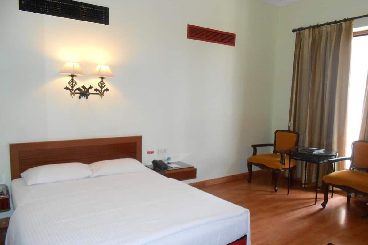 A hotel room with a large bed, two wall-mounted lamps, a desk with a chair, and a window with curtains.