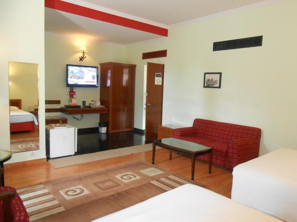 A hotel room with a bed, a red sofa, a small table, a television, and a kitchenette.