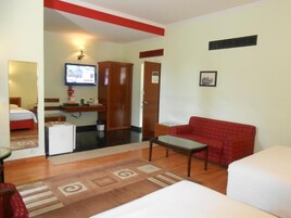 A hotel room with a bed, a red sofa, a small table, a television, and a kitchenette.
